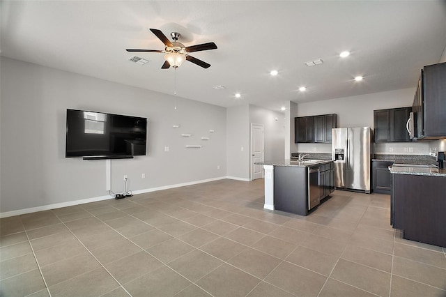 kitchen with appliances with stainless steel finishes, a kitchen island with sink, light tile patterned floors, ceiling fan, and light stone countertops