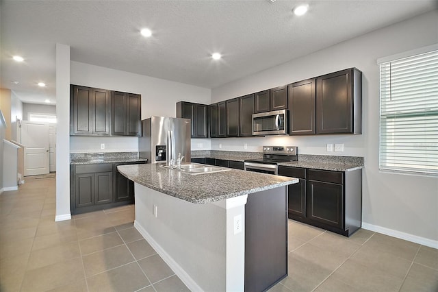 kitchen with sink, a center island with sink, stainless steel appliances, dark brown cabinetry, and light tile patterned flooring