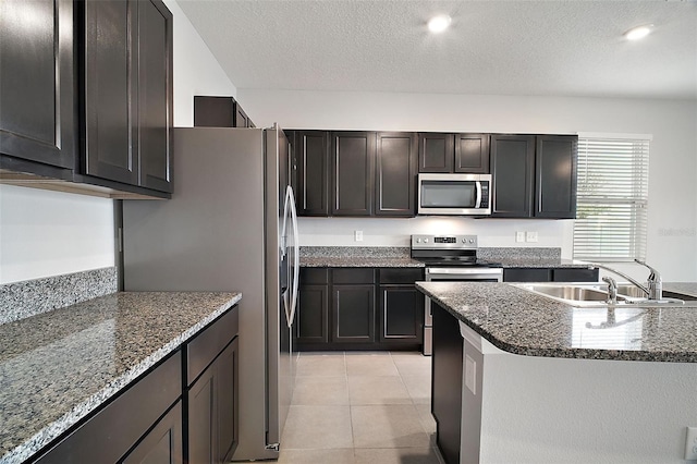 kitchen with sink, light tile patterned floors, stainless steel appliances, a textured ceiling, and dark stone counters