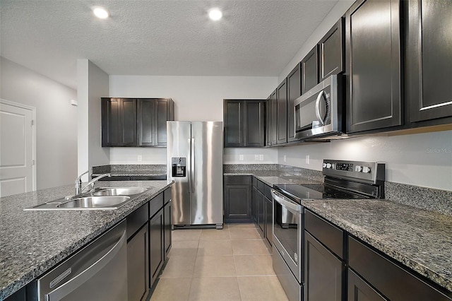 kitchen with sink, appliances with stainless steel finishes, a textured ceiling, light tile patterned flooring, and dark stone counters