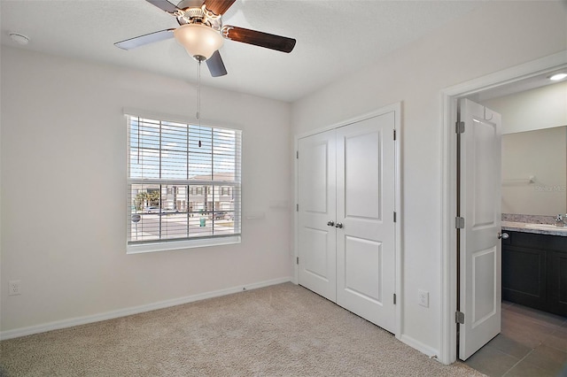 unfurnished bedroom featuring ceiling fan, light colored carpet, sink, and a closet