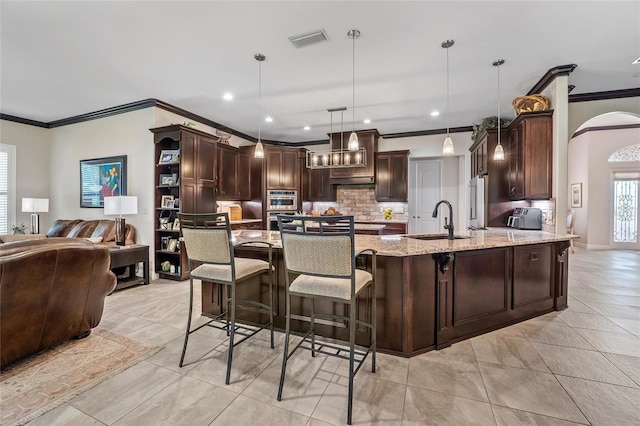 kitchen featuring a kitchen bar, sink, hanging light fixtures, light stone countertops, and decorative backsplash