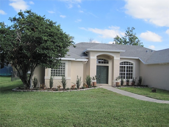 ranch-style house featuring roof with shingles, a front yard, and stucco siding