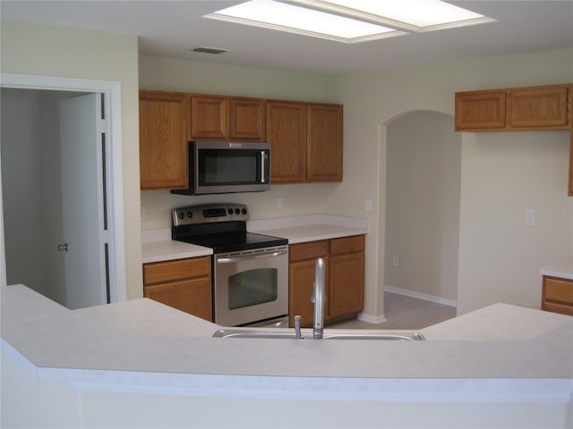 kitchen with stainless steel appliances, light countertops, brown cabinets, and a sink