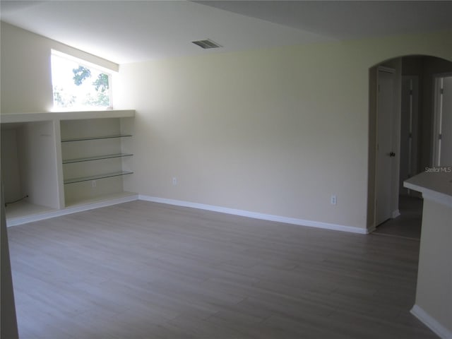 unfurnished room with baseboards, visible vents, arched walkways, and wood finished floors