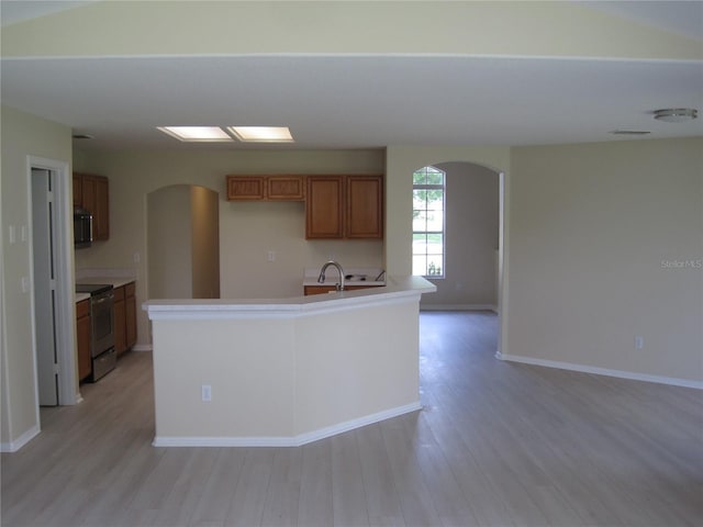 kitchen featuring arched walkways, brown cabinets, open floor plan, light wood-type flooring, and stainless steel electric range