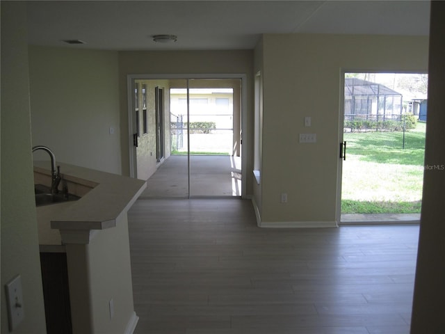 hallway featuring visible vents, a sink, baseboards, and wood finished floors