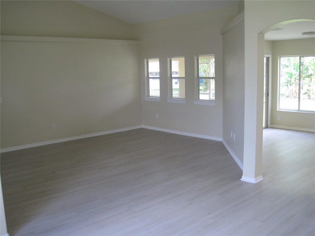 unfurnished room featuring vaulted ceiling, baseboards, arched walkways, and wood finished floors