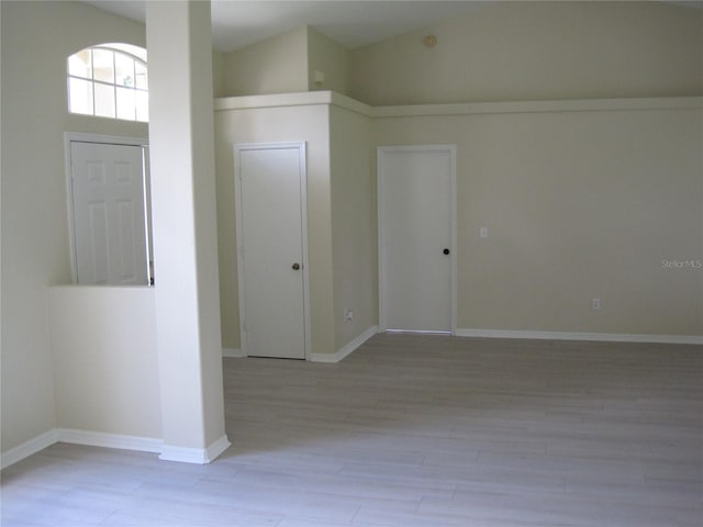 spare room featuring light wood-type flooring, baseboards, and high vaulted ceiling