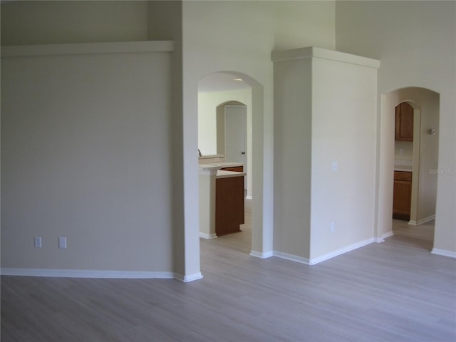 spare room featuring light wood-type flooring, baseboards, and arched walkways