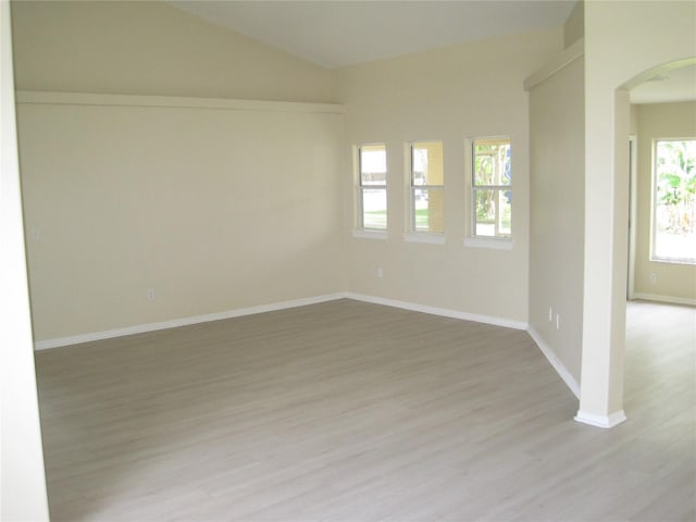 spare room with arched walkways, baseboards, lofted ceiling, and light wood finished floors