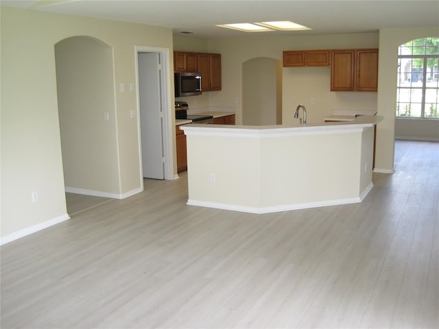 kitchen with brown cabinetry, arched walkways, stainless steel appliances, and light wood finished floors