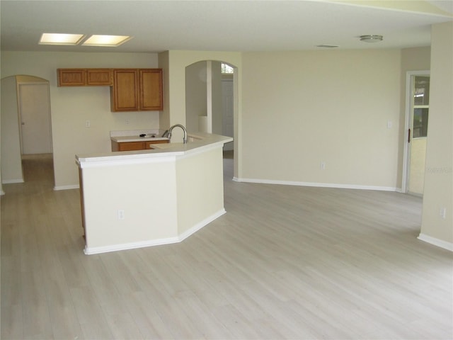 kitchen with arched walkways, light countertops, light wood finished floors, and brown cabinetry