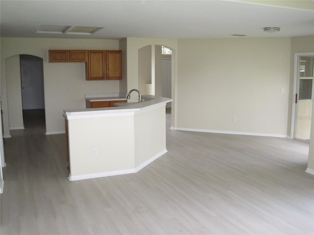 kitchen featuring arched walkways, brown cabinets, and light wood finished floors