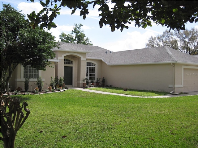 view of front of property featuring a front lawn, an attached garage, a shingled roof, and stucco siding