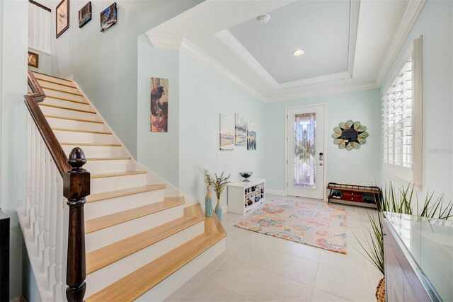 foyer entrance with crown molding, light tile patterned flooring, and a tray ceiling