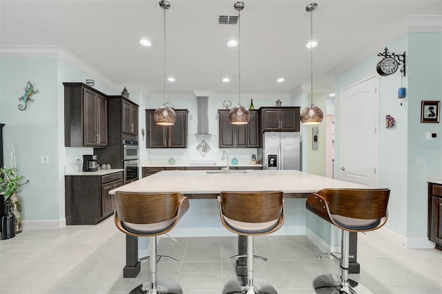 kitchen featuring a large island, appliances with stainless steel finishes, dark brown cabinetry, decorative light fixtures, and wall chimney exhaust hood