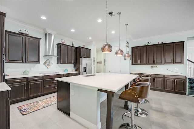 kitchen featuring pendant lighting, stainless steel fridge, a kitchen breakfast bar, wall chimney range hood, and a center island with sink