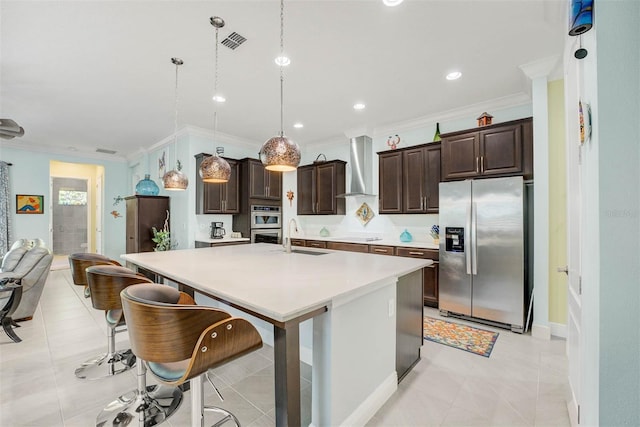 kitchen featuring appliances with stainless steel finishes, a breakfast bar area, hanging light fixtures, a center island with sink, and wall chimney exhaust hood