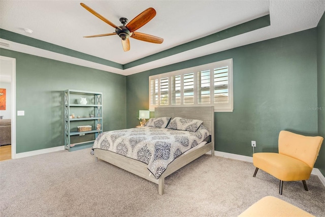 bedroom with ceiling fan, carpet flooring, and a raised ceiling