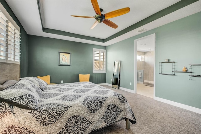 bedroom featuring ceiling fan, ensuite bathroom, a tray ceiling, and carpet