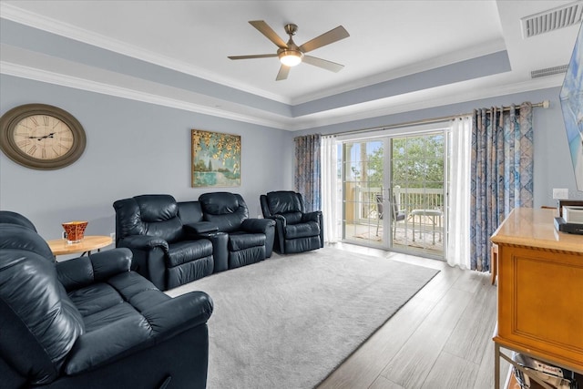 living room with crown molding, a tray ceiling, ceiling fan, and light wood-type flooring