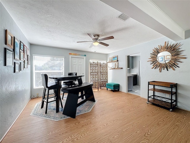 dining space with ceiling fan, light wood-type flooring, and a textured ceiling