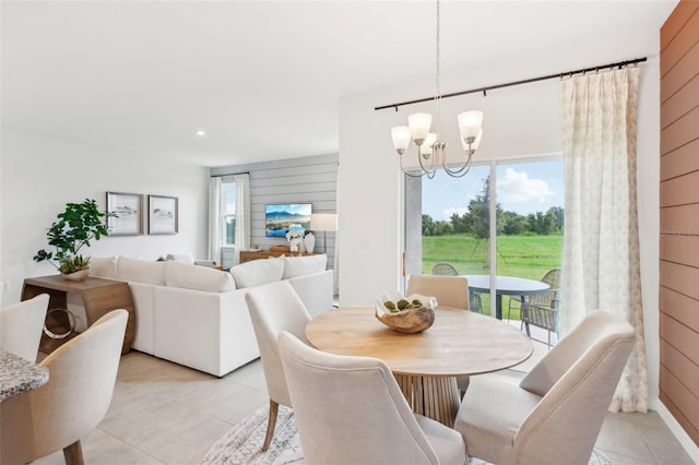 dining space with wooden walls, a chandelier, light tile patterned floors, and a wealth of natural light