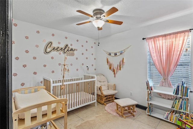 bedroom featuring ceiling fan, a nursery area, tile patterned floors, and a textured ceiling