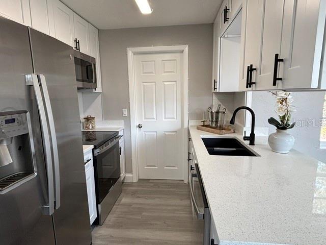 kitchen with sink, stainless steel appliances, light stone counters, light hardwood / wood-style floors, and white cabinets