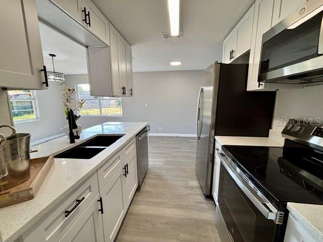 kitchen featuring sink, light stone counters, light wood-type flooring, stainless steel appliances, and white cabinets