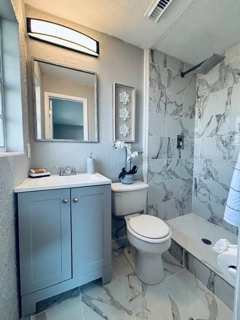 bathroom featuring a tile shower, vanity, toilet, and a textured ceiling