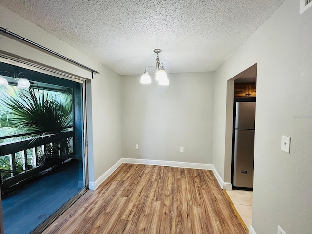 unfurnished dining area with an inviting chandelier, a textured ceiling, and light hardwood / wood-style floors