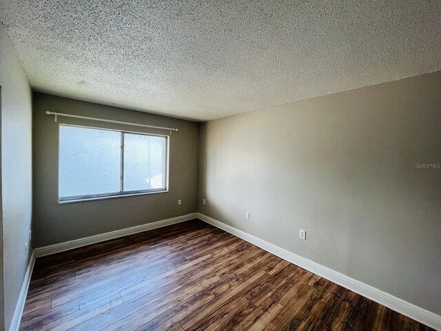 empty room with dark wood-type flooring and a textured ceiling