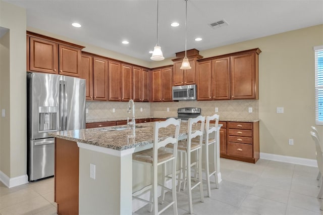 kitchen with appliances with stainless steel finishes, decorative light fixtures, an island with sink, sink, and light stone countertops