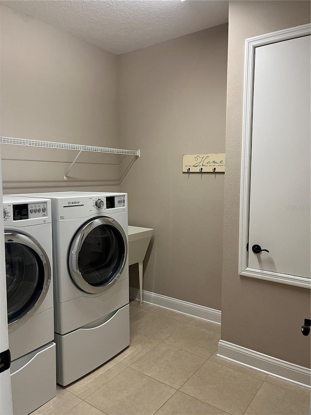 laundry room featuring washer and clothes dryer, a textured ceiling, and light tile patterned floors