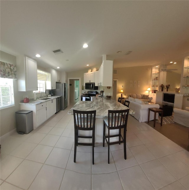 kitchen with appliances with stainless steel finishes, a breakfast bar, white cabinetry, light tile patterned floors, and kitchen peninsula