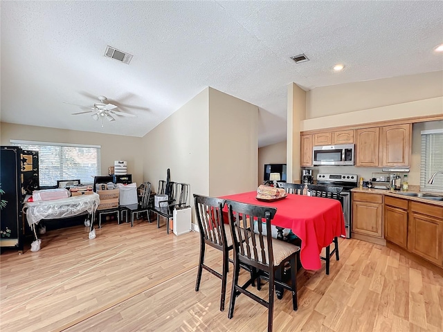 dining room with vaulted ceiling, sink, a textured ceiling, and light hardwood / wood-style flooring