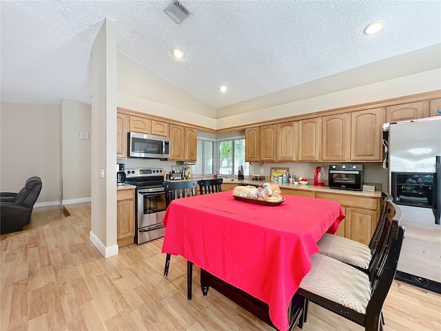 kitchen featuring light hardwood / wood-style flooring, vaulted ceiling, a textured ceiling, and appliances with stainless steel finishes