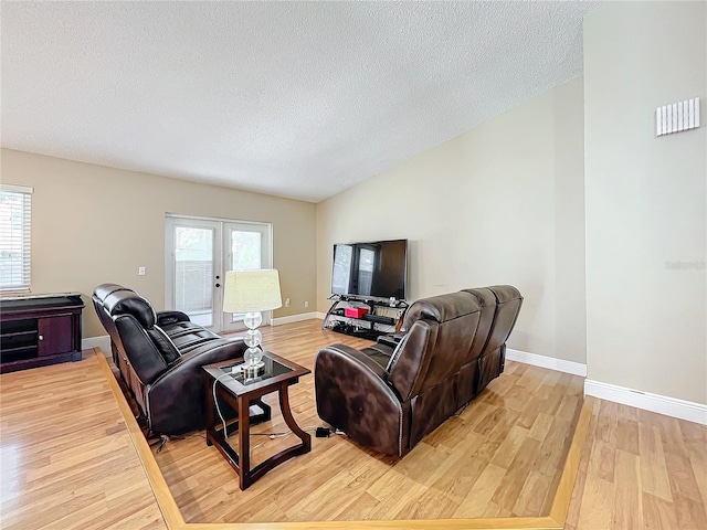 living room featuring a healthy amount of sunlight, a textured ceiling, light hardwood / wood-style floors, and french doors