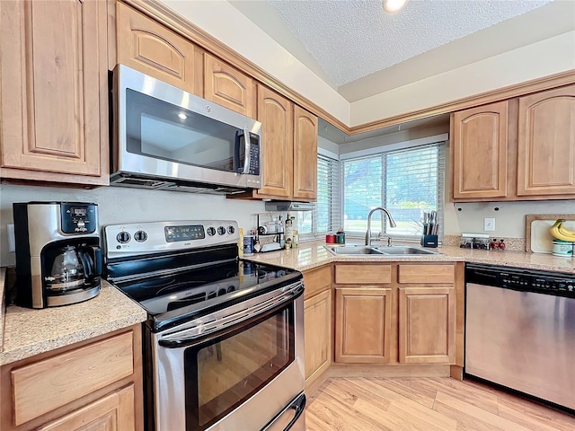 kitchen with sink, light hardwood / wood-style floors, stainless steel appliances, light stone countertops, and a textured ceiling