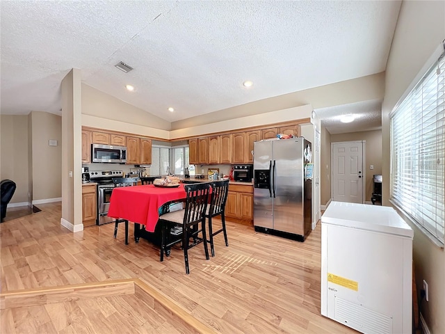 kitchen with lofted ceiling, stainless steel appliances, a center island, and light wood-type flooring