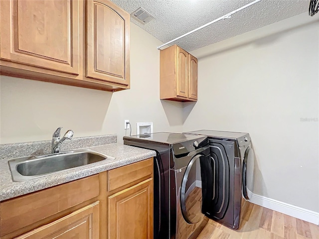 washroom with sink, cabinets, independent washer and dryer, light hardwood / wood-style floors, and a textured ceiling