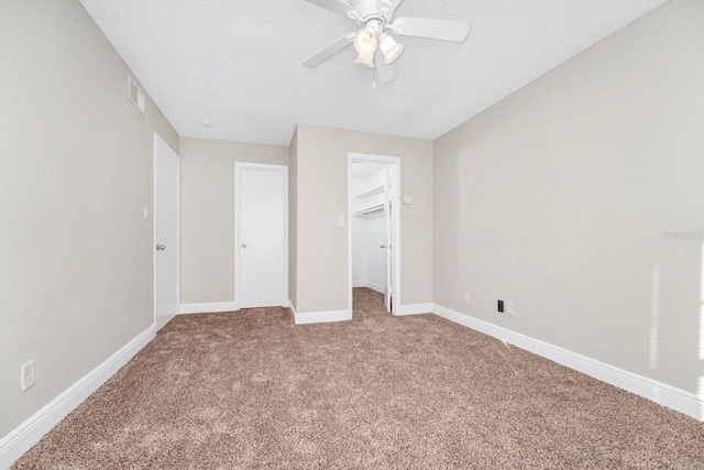 unfurnished bedroom with carpet floors, a walk in closet, ceiling fan, a textured ceiling, and a closet