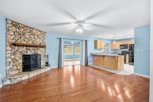 unfurnished living room with ceiling fan, a stone fireplace, light hardwood / wood-style flooring, and a textured ceiling