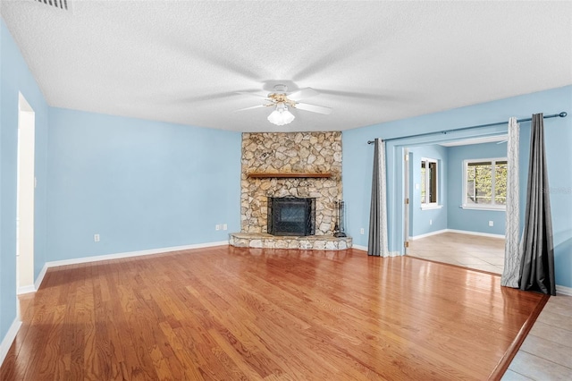 unfurnished living room with ceiling fan, a stone fireplace, a textured ceiling, and light hardwood / wood-style floors