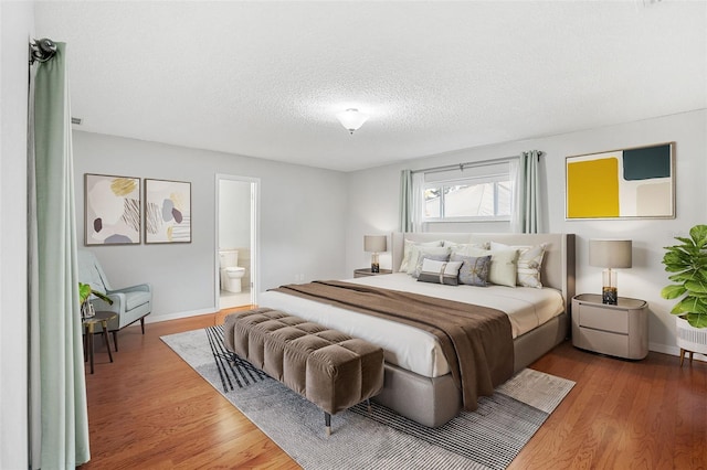 bedroom with wood-type flooring, a textured ceiling, and ensuite bath