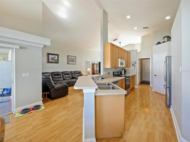 kitchen featuring sink, high vaulted ceiling, kitchen peninsula, stainless steel appliances, and light hardwood / wood-style floors