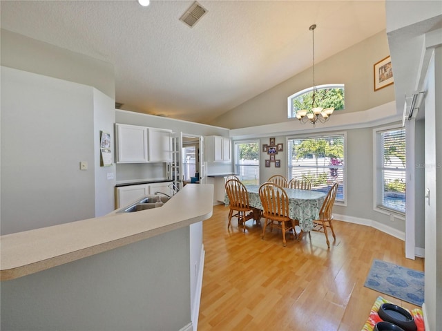 dining room with lofted ceiling, sink, light hardwood / wood-style floors, a textured ceiling, and a chandelier