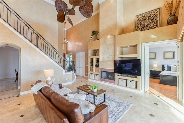 living room with a high ceiling, crown molding, ceiling fan, and built in shelves